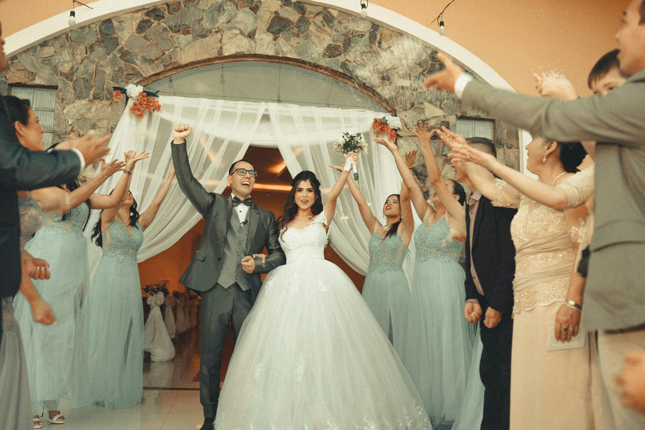 Home Cheerful newlyweds celebrating their wedding with guests applauding in stylish attire.