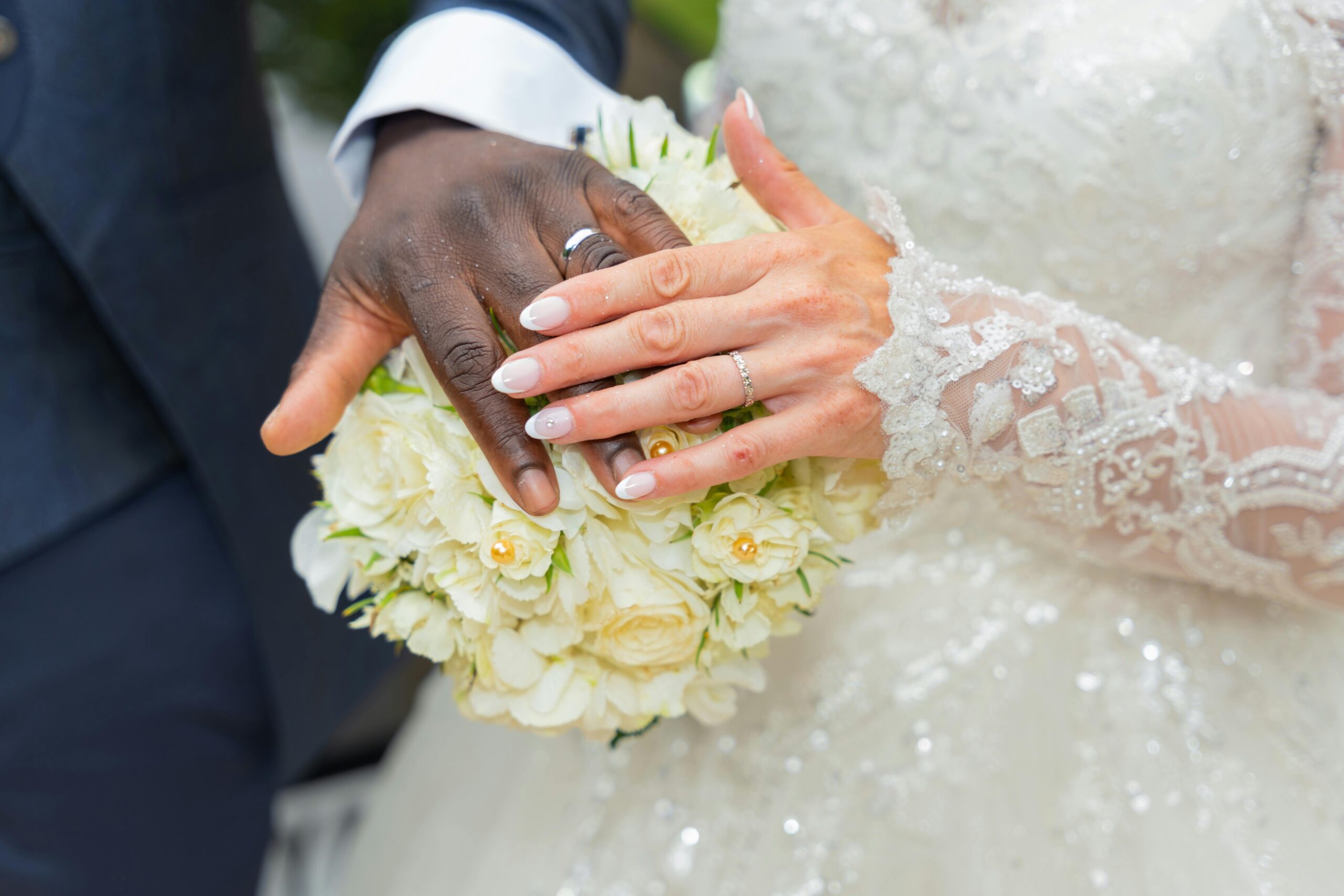 About Interracial couple's hands with wedding rings and bouquet, symbolizing love and unity.