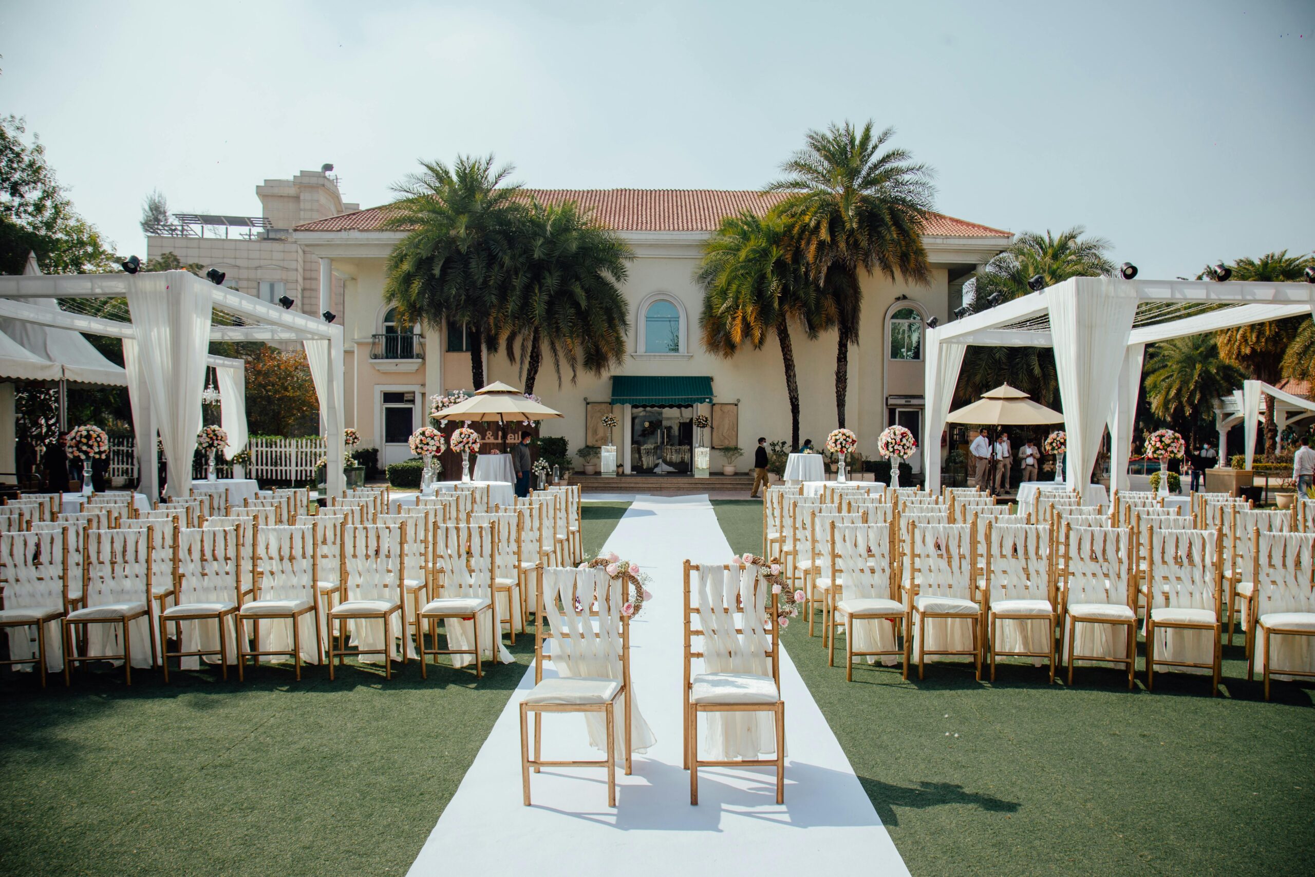 Home Beautiful outdoor wedding ceremony setup with rows of decorated chairs facing a luxurious villa.