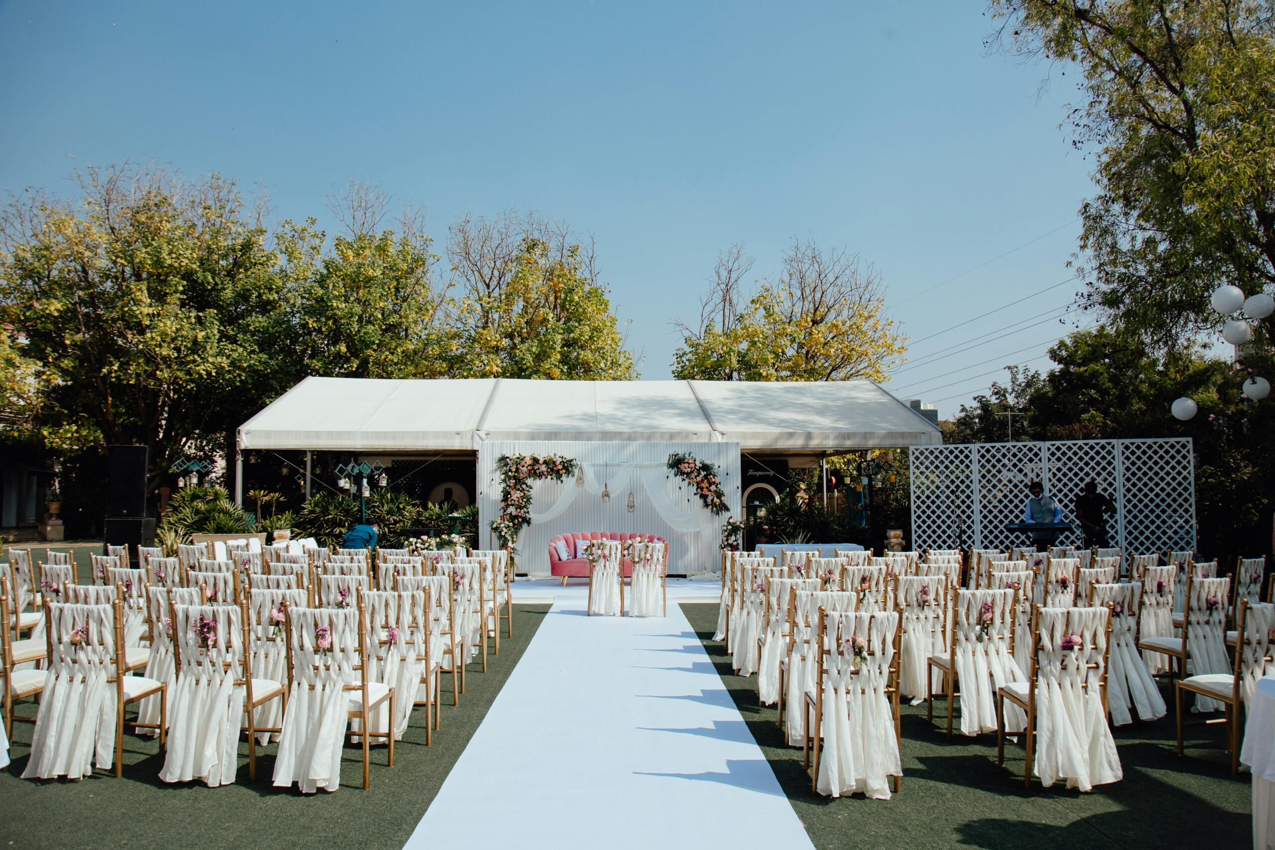 Services Elegant outdoor wedding setup with decorated chairs and floral arrangements under a clear blue sky.